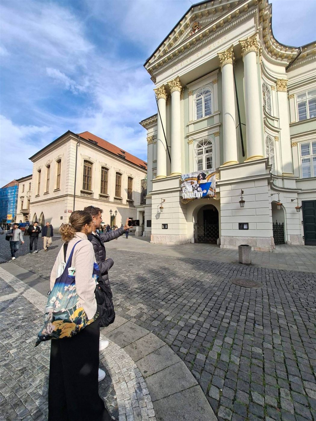 Two players hold up the phone in front of the Estates Theatre