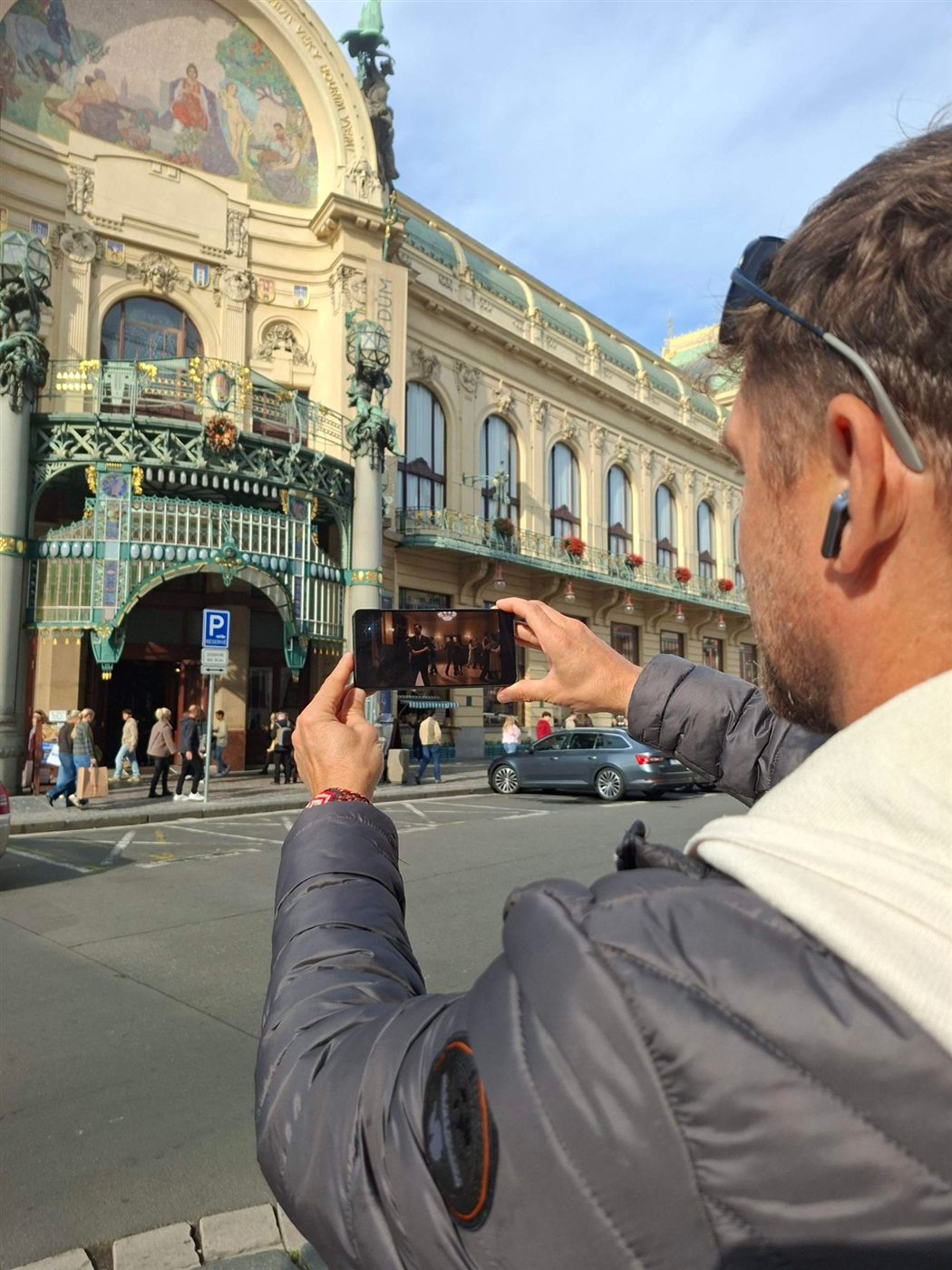 A player watches the Municipal House scene on his phone in front of the building